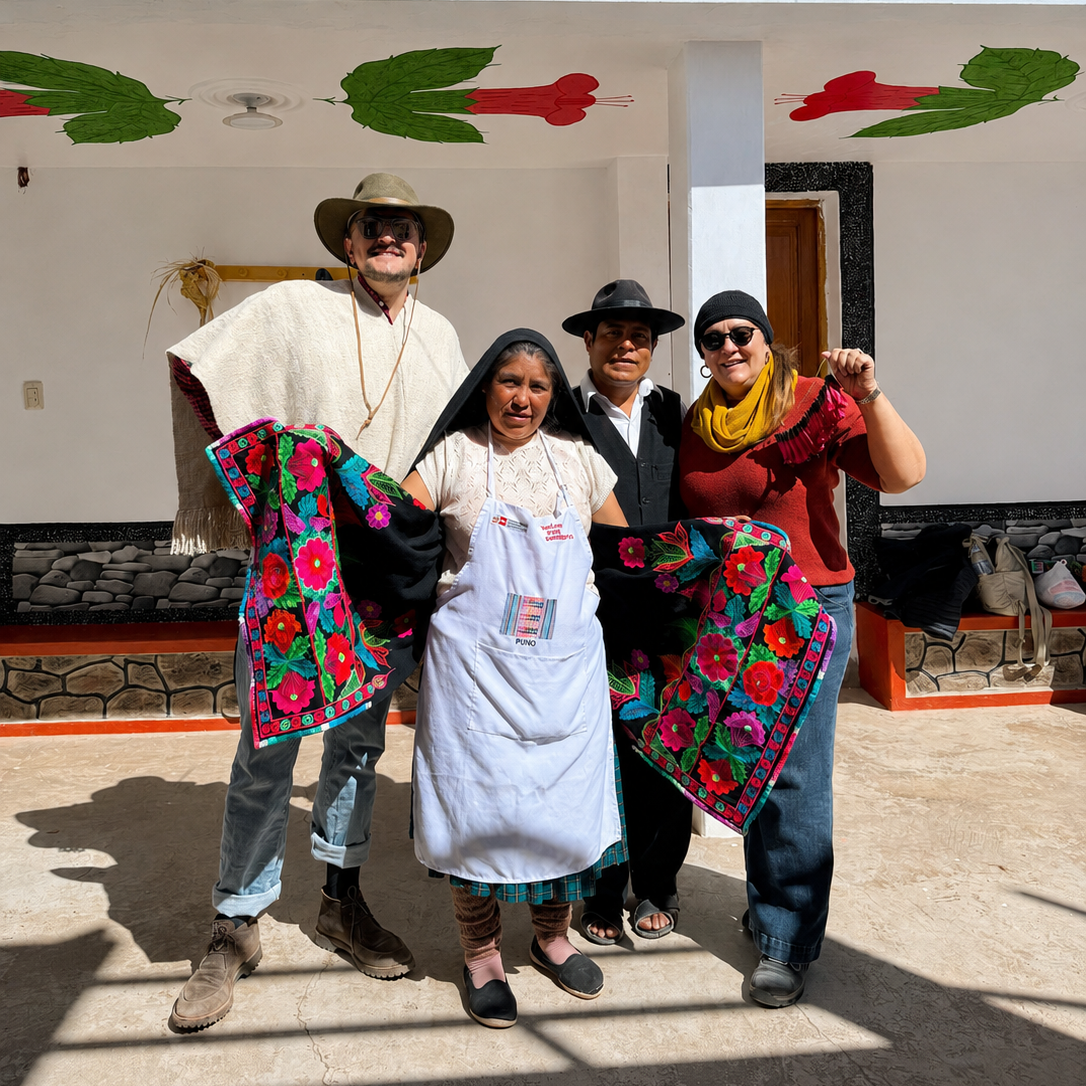 Four people standing outdoors in front of a white building with colorful mural details, each holding up a vibrant floral embroidered blanket or scarf. The group is dressed in casual and traditional-style clothing from Lake Titicaca, Peru.