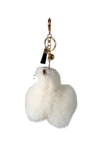 A fluffy white Alpaca fur keychain charm shaped like a small animal, attached to a gold-tone key ring, lobster clasp, and small black tassel on a plain white background.