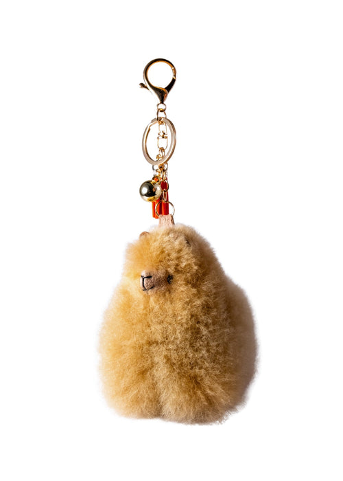A fluffy beige alpaca fur keychain charm with a gold-tone lobster clasp, key ring, small bead, and bell, shown on a plain white background.